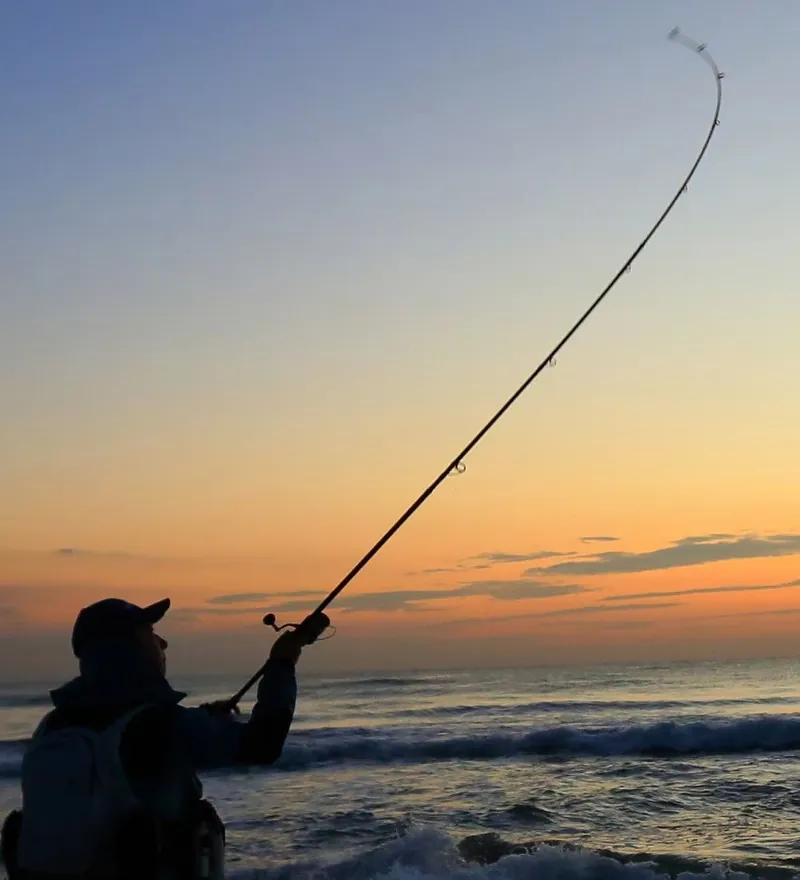 Pescador lanzando con caña de spinning al atardecer